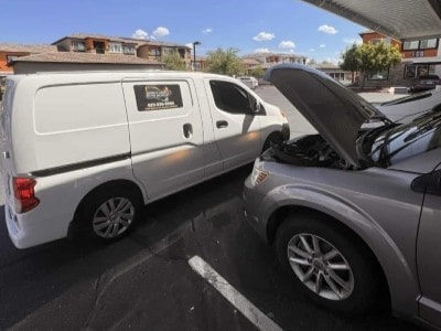 A Mobile Man Auto Repair service van parked beside a customer's car with the hood up, performing an on-site repair in a West Valley driveway